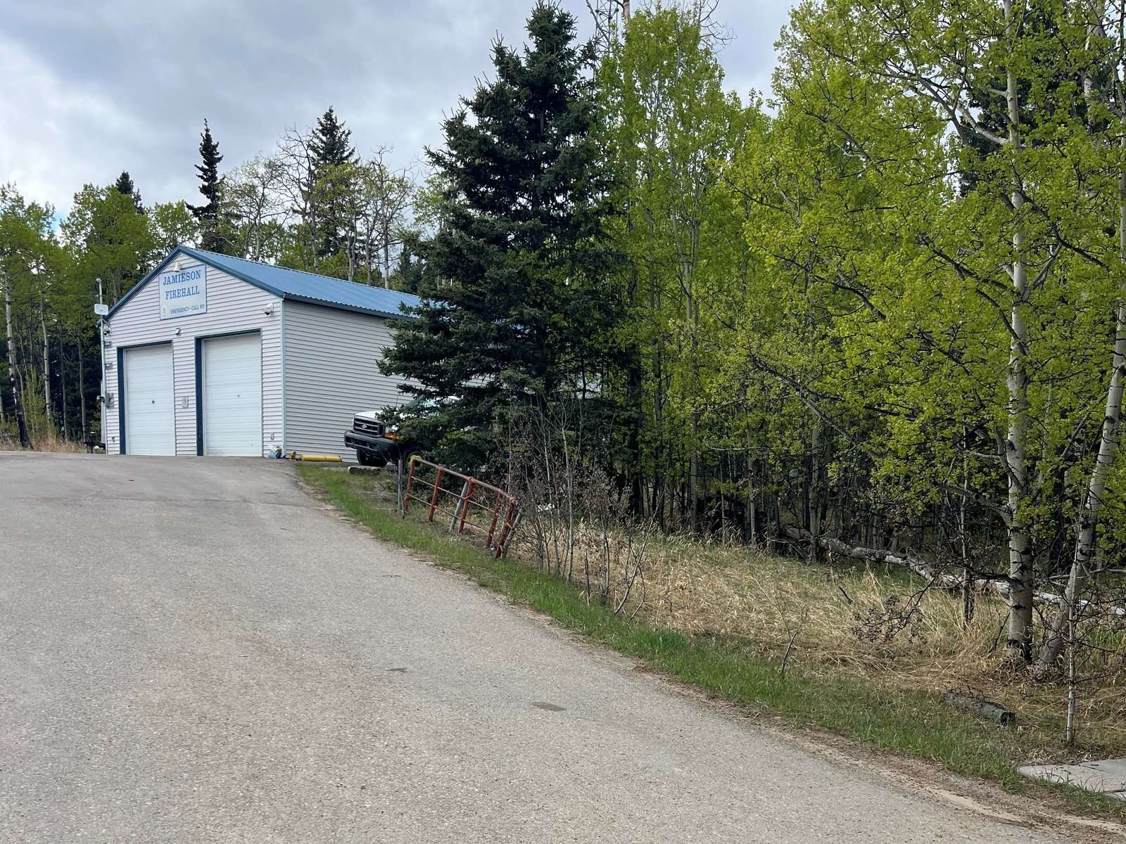 The existing two-bay Jamieson Road fire hall among aspen and spruce, May 2025